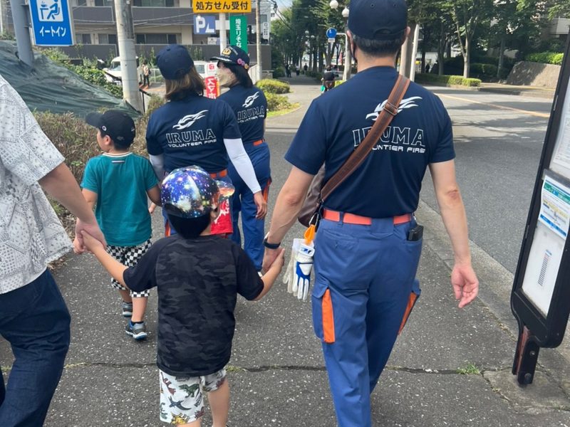 制服姿の大人が子どもたちと手をつないで歩く後ろ姿